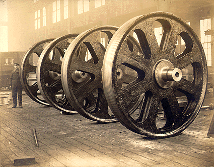 Scanned photo of worker standing next to giant gears.